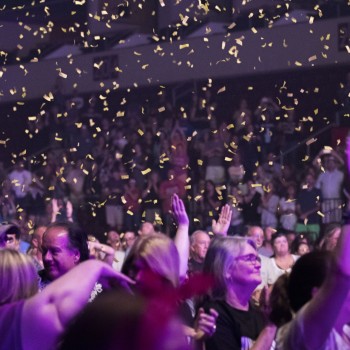 Picture of the crowd at a concert with hands up in the air.