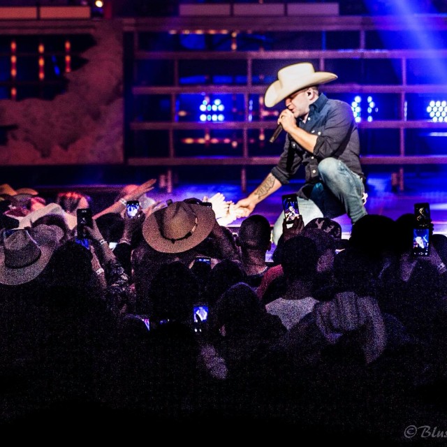 Justin Moore shaking a fans hand at the stage edge while singing.